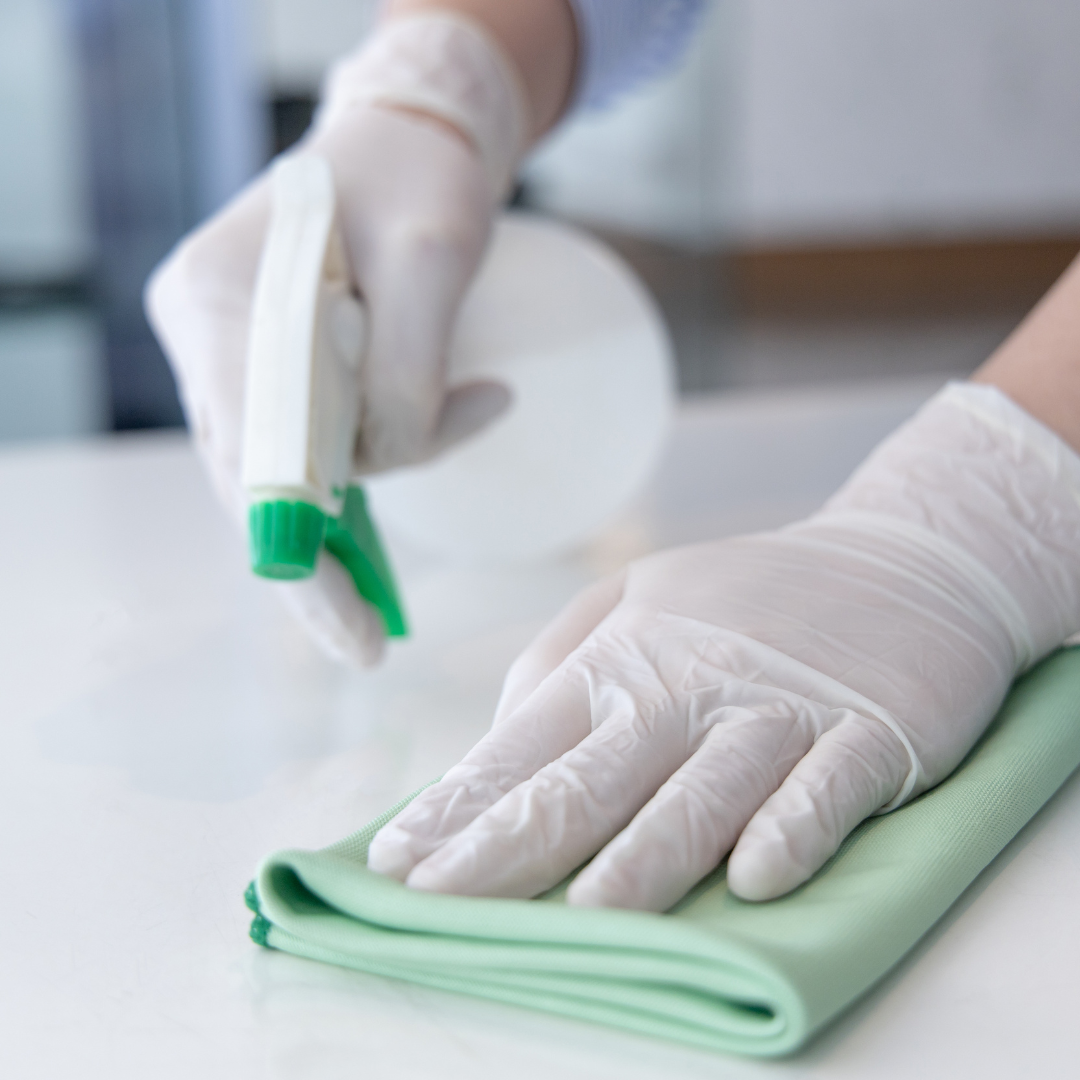 a person's hands cleaning the office's surface with sprayer and cloth wearing gloves